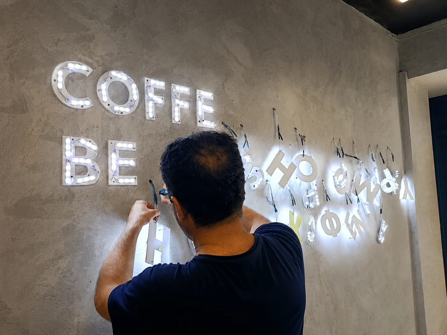 Монтаж световых букв COFFEE BE на стену — мастер прокладывает провода